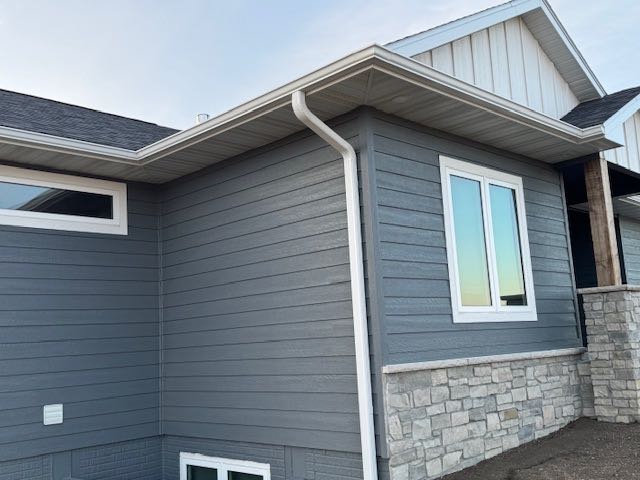 A modern house exterior with blue-gray siding, white trim, and stone accents. Large windows reflect a blue sky, creating a clean and serene look.