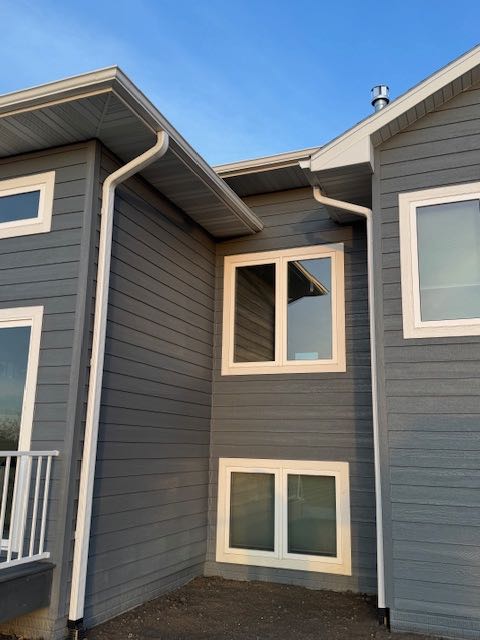 Modern house corner with gray siding, white trim, and multiple windows under a clear blue sky. The scene conveys a sense of calm and order.