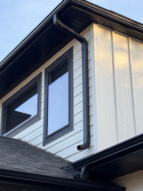 Close-up of a modern house exterior featuring sleek black-framed windows and a black drainpipe against light beige vertical siding, with a peaceful tone.
